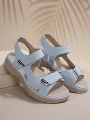 Sandali estivi da donna in pelle azzurra con suola piatta, chiusura a strappo e dettagli metallici. Calzature comode e alla moda per l'estate.