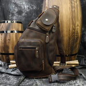 Zaino a tracolla in pelle marrone con tasche multiple, design vintage. Sfondo con barili di legno. Accessorio moda uomo, stile retrò.