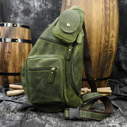 Zaino a tracolla in pelle verde con tasche multiple, design vintage. Sfondo con barili di legno. Accessorio moda uomo, stile retrò.
