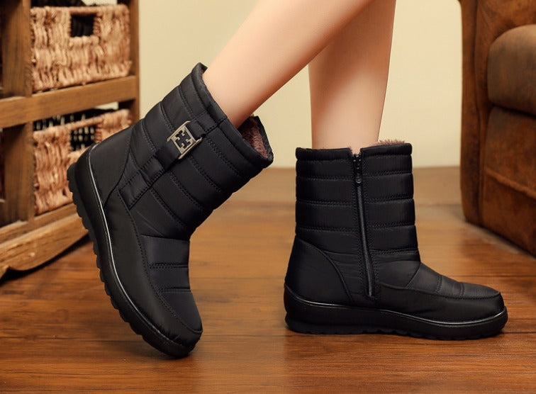 Stivali invernali neri imbottiti da donna, con cerniera laterale e fibbia, su pavimento in legno. Scarpe calde e impermeabili per l'inverno.