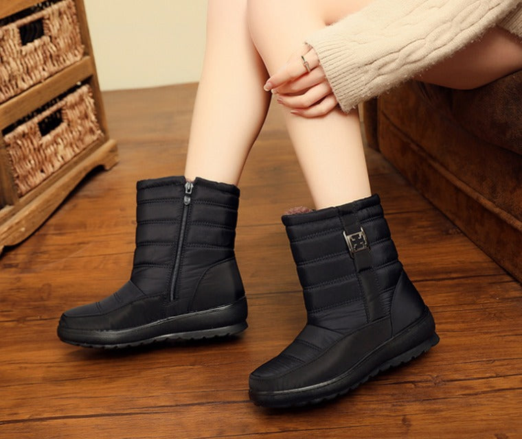 Stivali invernali neri da donna con cerniera, su pavimento in legno, indossati con maglione beige. Scarpe calde e impermeabili per l'inverno.