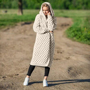 Donna con cardigan lungo a maglia beige con cappuccio, su strada sterrata. Moda autunnale, abbigliamento casual, stile confortevole.