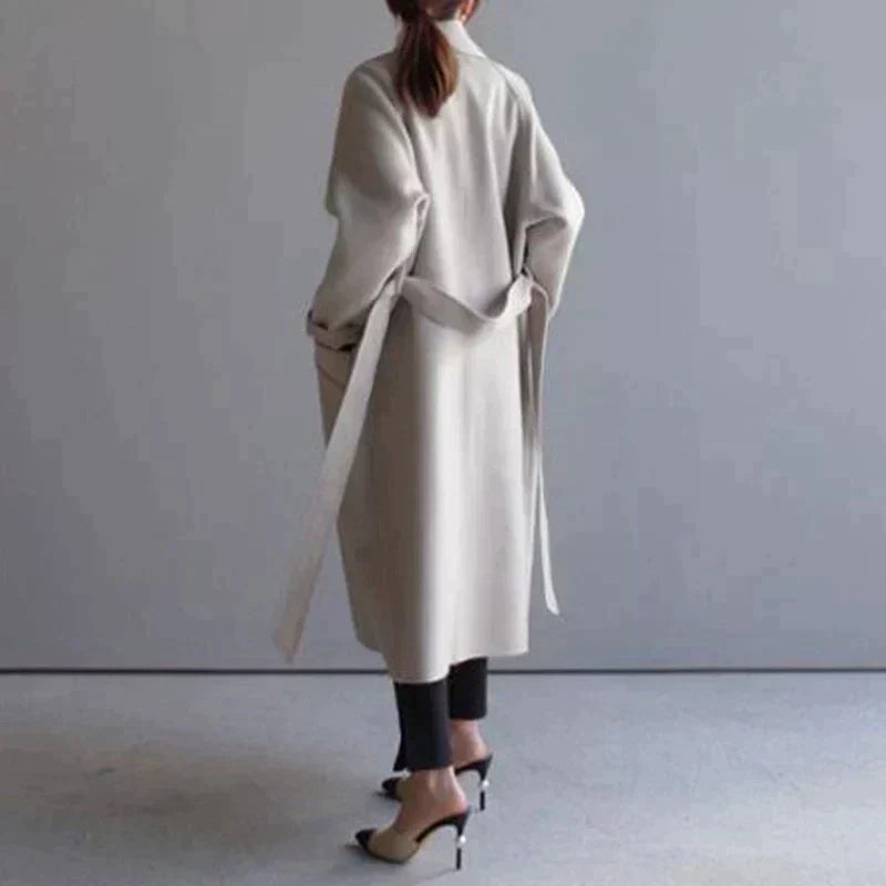 Cappotto lungo beige donna, design elegante, cintura in vita, abbinato a pantaloni neri e tacchi alti. Moda autunnale, stile minimalista.