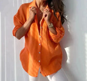 Camicia donna arancione a maniche lunghe, tessuto leggero, abbinata a pantaloni bianchi. Stile casual, moda femminile, abbigliamento estivo.