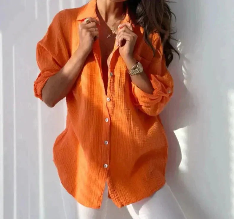 Camicia donna arancione a maniche lunghe, tessuto leggero, abbinata a pantaloni bianchi. Stile casual, moda femminile, abbigliamento estivo.