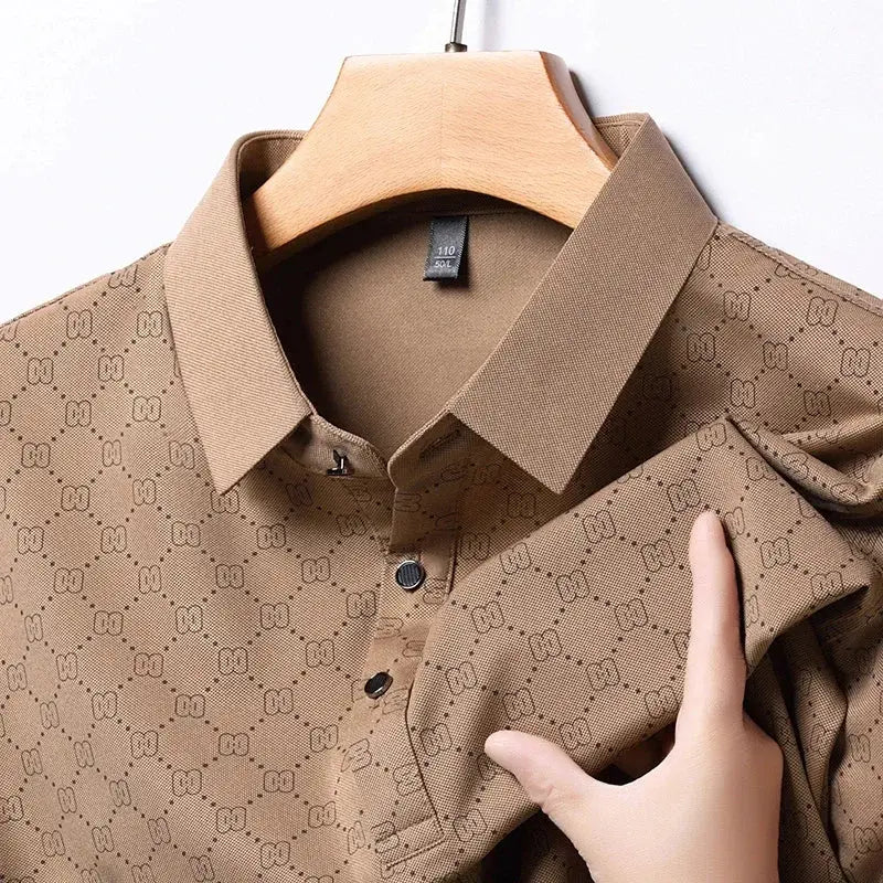 Camicia marrone a maniche lunghe con motivo geometrico, colletto classico e bottoni, appesa su gruccia di legno. Tessuto elegante e moderno.