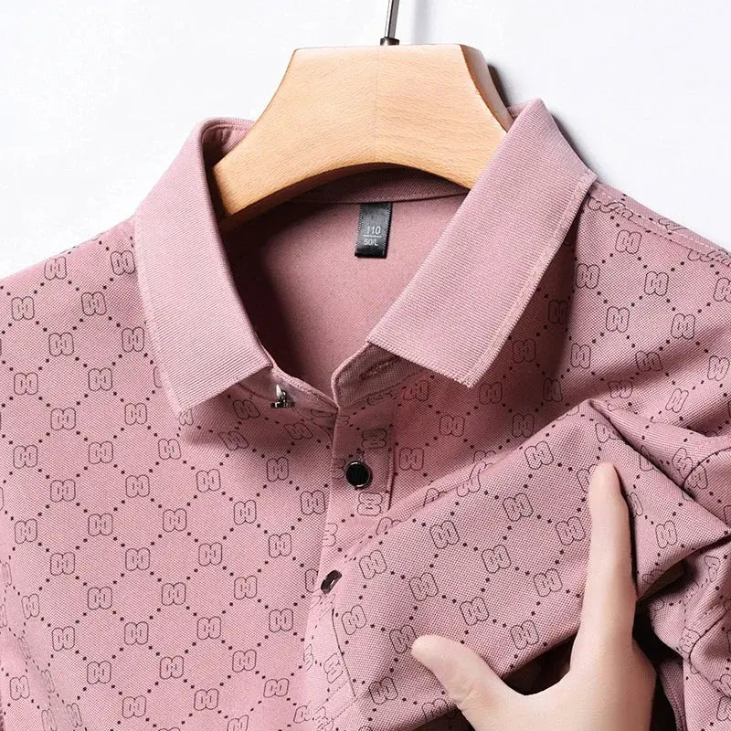 Camicia polo rosa con motivo geometrico, colletto classico e bottoni neri, appesa su gruccia di legno. Tessuto elegante e moderno.