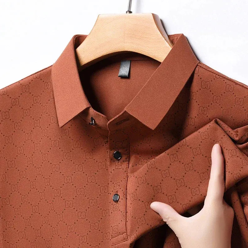 Camicia marrone a maniche lunghe con motivo geometrico, colletto classico e bottoni neri, appesa su gruccia di legno. Tessuto elegante e moderno.