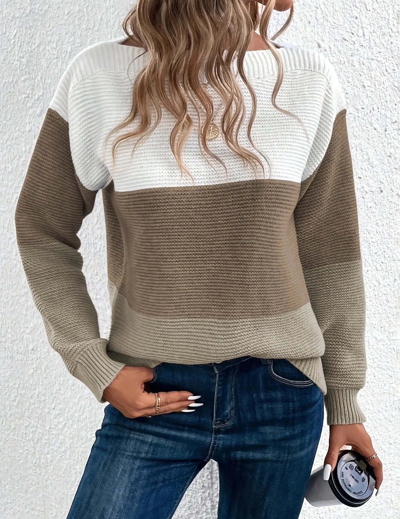 Maglione a righe bianche e marroni, donna con capelli ondulati, jeans blu, tiene una tazza. Moda autunnale casual, abbigliamento femminile trendy.