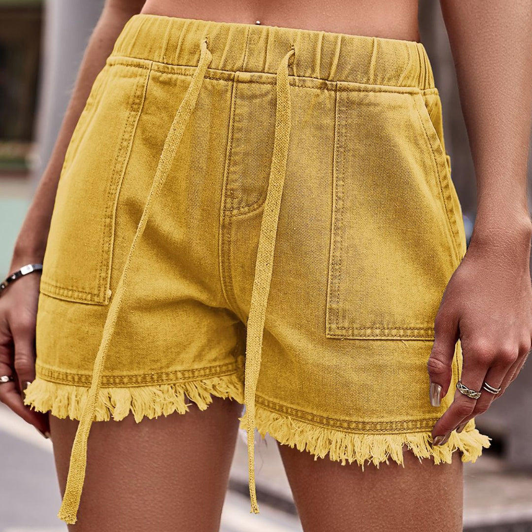 Shorts gialli in denim con frange, vita alta e laccetti, indossati da una donna. Stile casual estivo, moda femminile trendy.