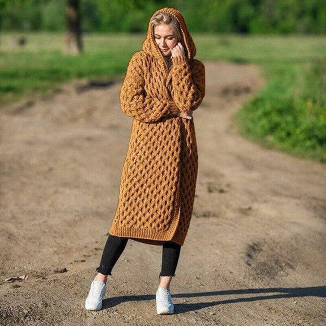Donna con abito lungo a maglia marrone, cappuccio, su strada sterrata. Moda autunnale, abbigliamento casual, stile confortevole.