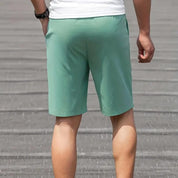 Pantaloncini sportivi verdi da uomo, tessuto leggero, indossati all'aperto. Ideali per attività fisica e tempo libero.