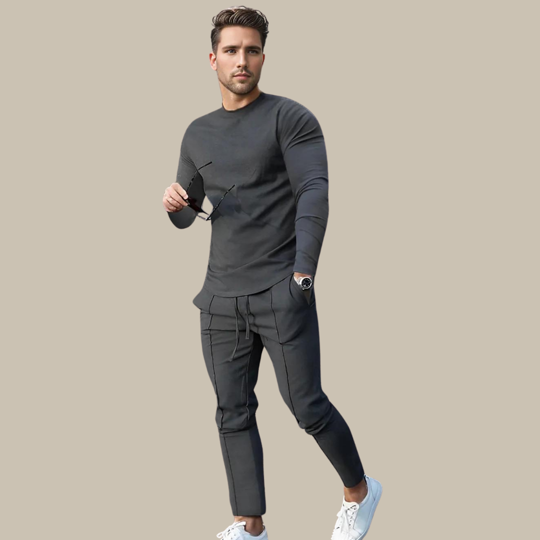Uomo in abbigliamento casual elegante, indossa maglia e pantaloni grigi, scarpe bianche, orologio nero, occhiali da sole in mano. Moda maschile moderna.