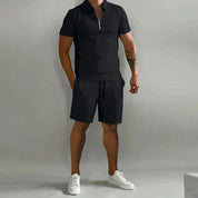 Uomo in completo estivo nero, polo con zip e pantaloncini, scarpe bianche. Moda casual maschile, abbigliamento estivo elegante.