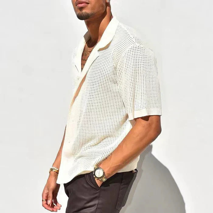 Camicia uomo bianca traforata a maniche corte, stile casual estivo, indossata con pantaloni scuri. Accessori: orologio e bracciali dorati.