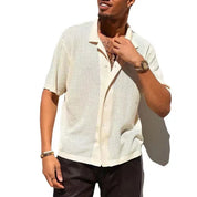 Camicia uomo estiva a maniche corte, colore beige, tessuto traforato, stile casual, abbinata a pantaloni scuri. Look moderno e fresco.