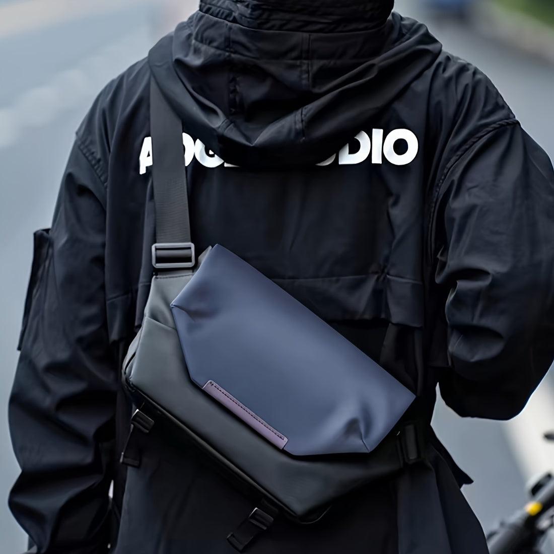 Giacca nera con scritta bianca e borsa a tracolla blu scuro, design moderno, moda urbana, accessorio unisex, stile casual, strada di città.