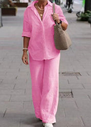 Donna con camicia e pantaloni rosa, borsa a tracolla beige, cammina su marciapiede. Moda estiva casual, abbigliamento femminile elegante.