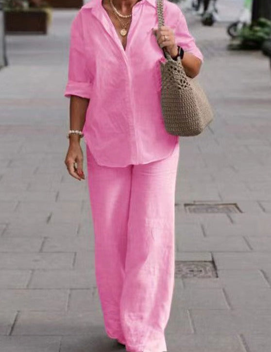 Donna con camicia e pantaloni rosa, borsa a tracolla beige, cammina su marciapiede. Moda estiva casual, abbigliamento femminile elegante.