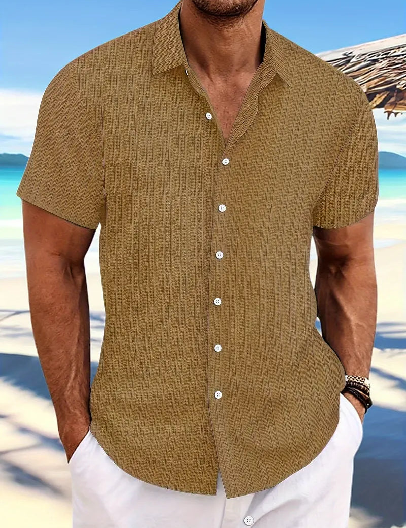 Camicia estiva da uomo a maniche corte color beige, con bottoni bianchi, indossata su spiaggia tropicale. Moda casual, abbigliamento estivo elegante.
