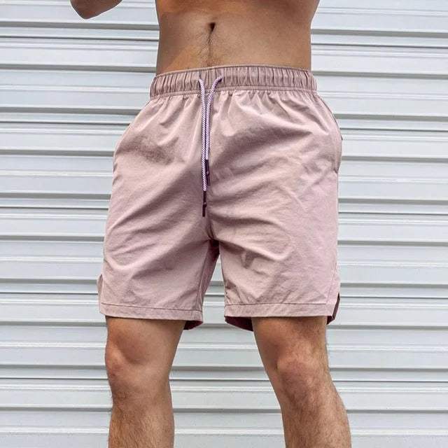 Shorts sportivi rosa da uomo, elastico in vita con cordino, davanti a una porta bianca. Abbigliamento estivo casual, moda fitness maschile.