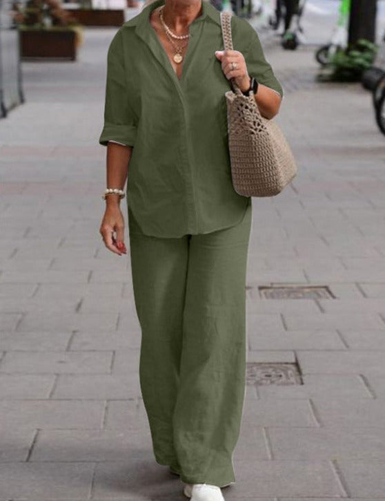 Donna con completo verde oliva, camicia e pantaloni larghi, borsa intrecciata beige, cammina su marciapiede urbano. Moda casual elegante.