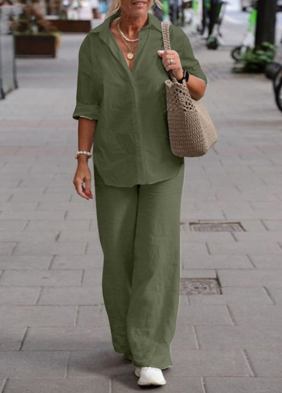 Donna con completo verde oliva, camicia a maniche lunghe e pantaloni larghi, borsa intrecciata beige, cammina su marciapiede cittadino.