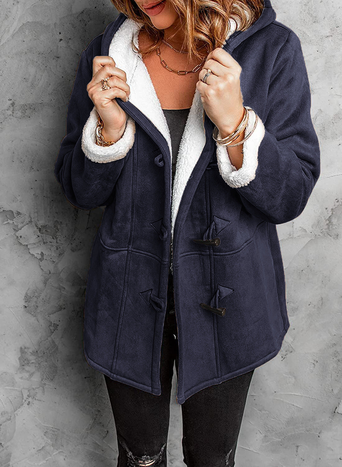 Donna con cappotto invernale blu scuro con fodera in pelliccia sintetica bianca, chiusura a alamari, su sfondo grigio. Moda femminile, abbigliamento caldo.