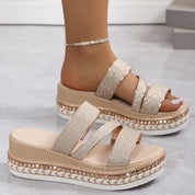Sandali platform donna con cinturini glitterati, suola intrecciata, colore oro, indossati su pavimento chiaro. Scarpe estive moda elegante.