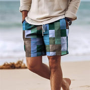 Uomo in spiaggia con pantaloncini patchwork colorati, maglione beige, orologio al polso. Moda estiva, abbigliamento casual maschile.
