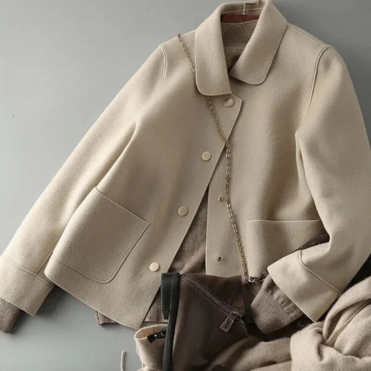 Giacca beige in lana con bottoni, tasche frontali e catena dorata. Moda autunno inverno, abbigliamento donna elegante e casual.