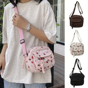 Borsa a tracolla rosa con motivo fragole, indossata da una persona. Disponibile in vari colori: marrone, bianco, nero. Accessorio moda casual.