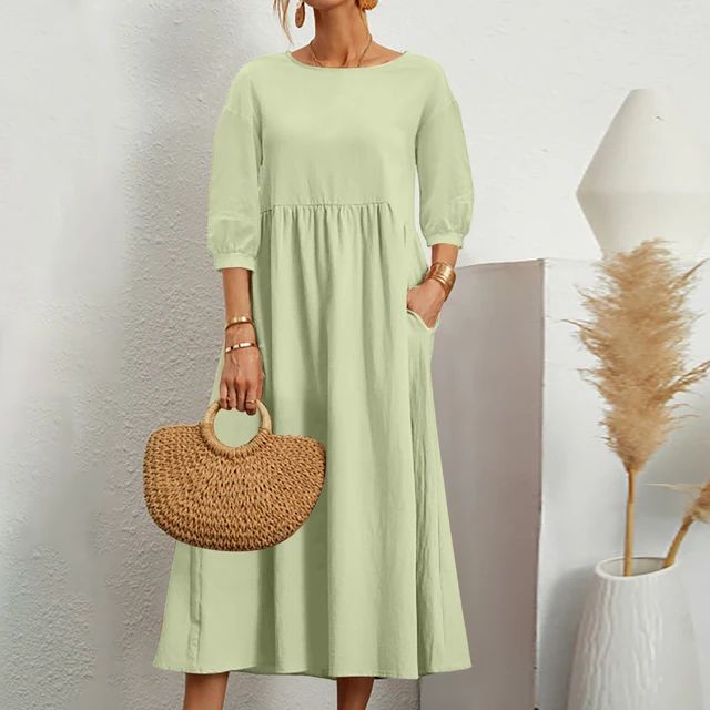 Abito lungo verde chiaro con maniche a tre quarti, tasche laterali, borsa in paglia, sfondo bianco minimalista, moda donna estiva elegante.