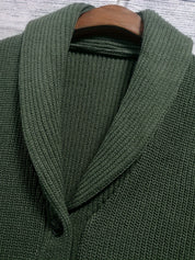 Cardigan verde in maglia a coste con colletto sciallato, chiusura a bottoni, su appendiabiti di legno. Maglione elegante e caldo per l'inverno.