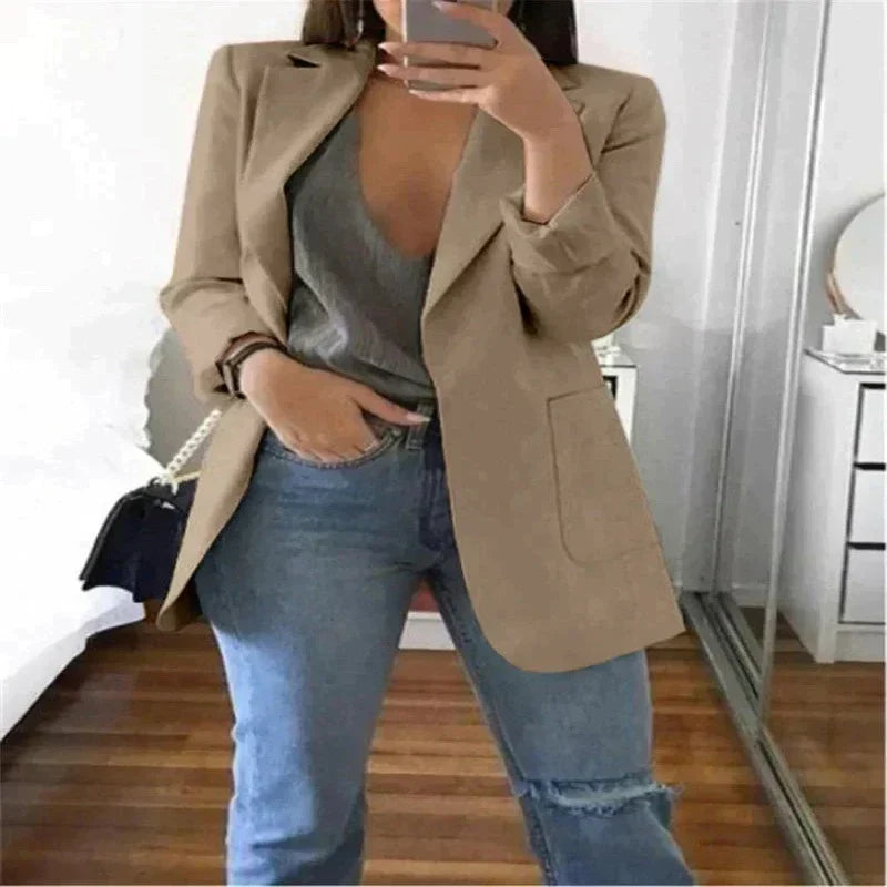 Donna in blazer beige, top grigio e jeans strappati, scatta selfie in camera moderna. Moda casual chic, abbigliamento femminile trendy.