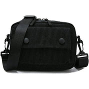 Borsa a tracolla nera in tessuto a coste, con tasca frontale e chiusura a bottoni. Design unisex, ideale per uso quotidiano e casual.