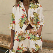 Donna con completo estivo floreale, camicia e pantaloncini coordinati, sfondo neutro. Moda donna, abbigliamento casual, stile tropicale.