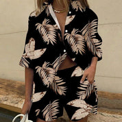 Donna con completo estivo nero a foglie tropicali beige, camicia e pantaloncini coordinati, moda casual, accessori eleganti, sfondo neutro.