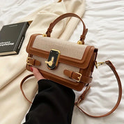 Borsa a tracolla elegante in pelle marrone e tessuto beige, con fibbia dorata, su sfondo di tessuto bianco e libro nero. Accessorio moda donna.