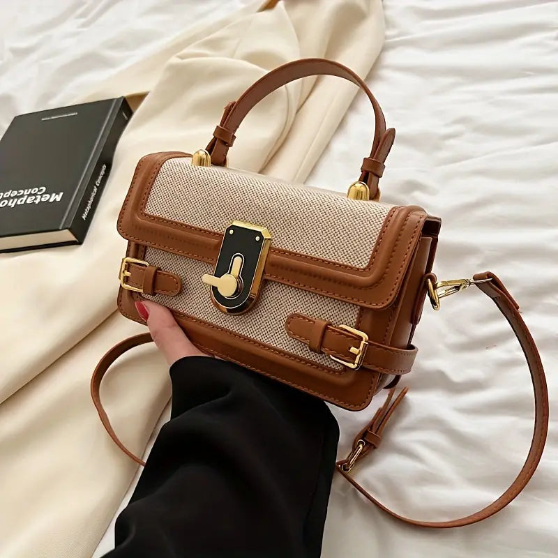 Borsa a tracolla elegante in pelle marrone e tessuto beige, con fibbia dorata, su sfondo di tessuto bianco e libro nero. Accessorio moda donna.
