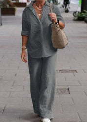 Donna con camicia e pantaloni grigi, borsa a maglia beige, cammina su marciapiede. Moda casual, abbigliamento estivo, accessori eleganti.