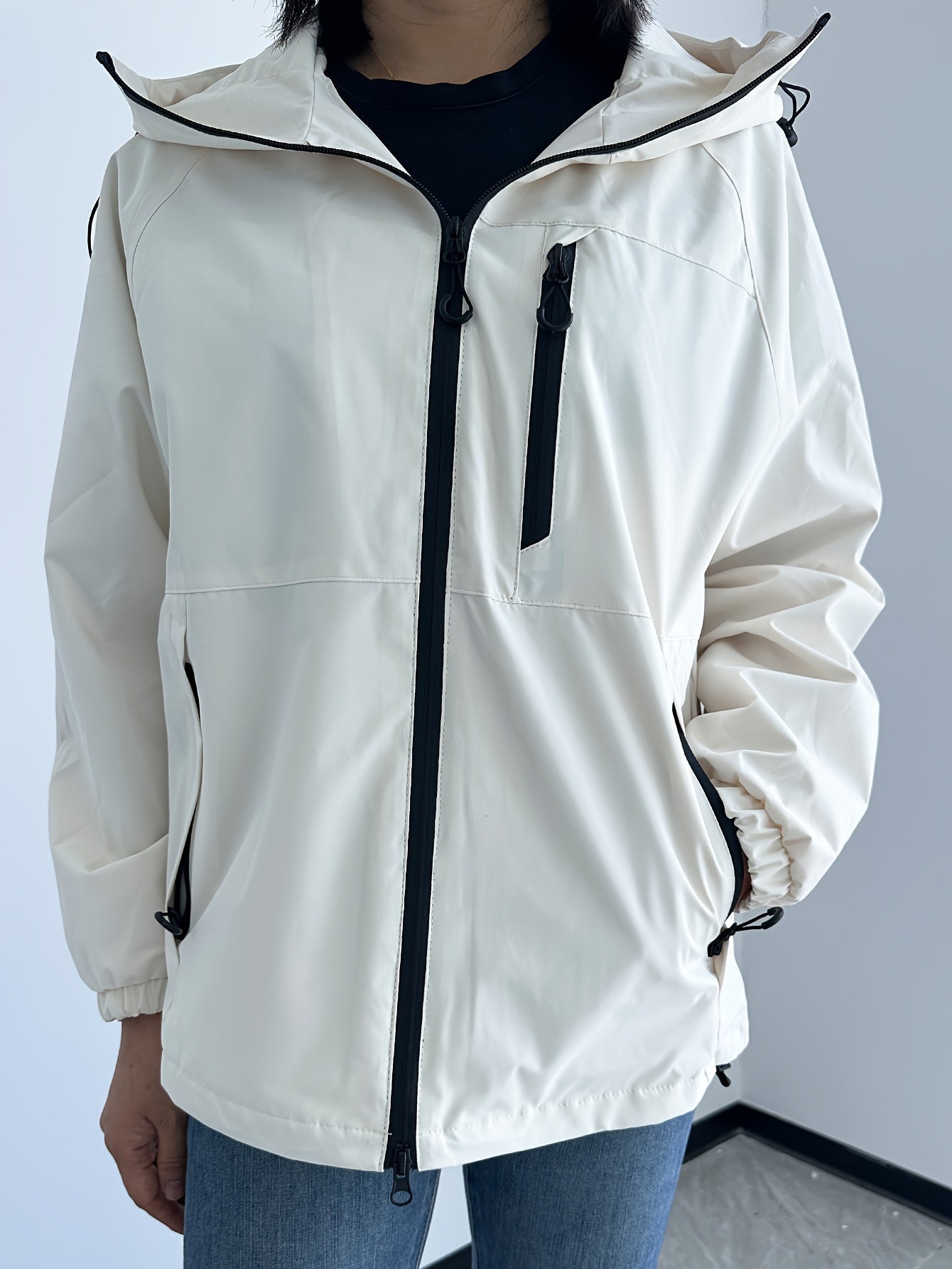 Giacca a vento bianca da donna con cappuccio, zip frontale nera, tasche laterali e polsini elasticizzati. Abbigliamento casual, moda autunnale.