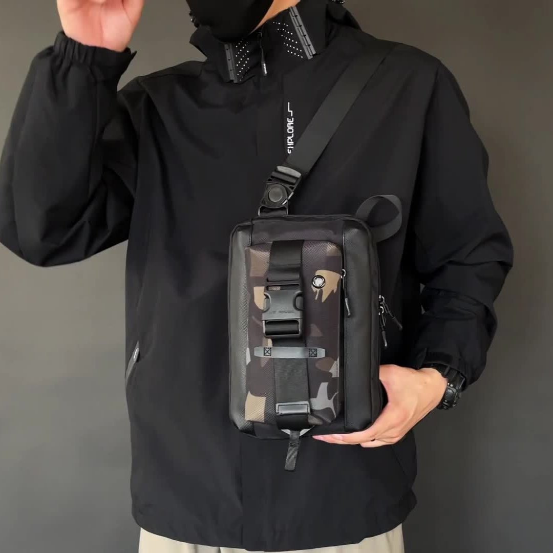 Uomo con giacca nera indossa borsa a tracolla mimetica, stile urbano. Accessorio moda maschile, pratico per viaggi e uso quotidiano.