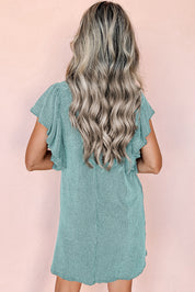 Donna con capelli ondulati biondi indossa un abito verde menta a maniche corte, sfondo rosa. Moda estiva, abbigliamento casual elegante.