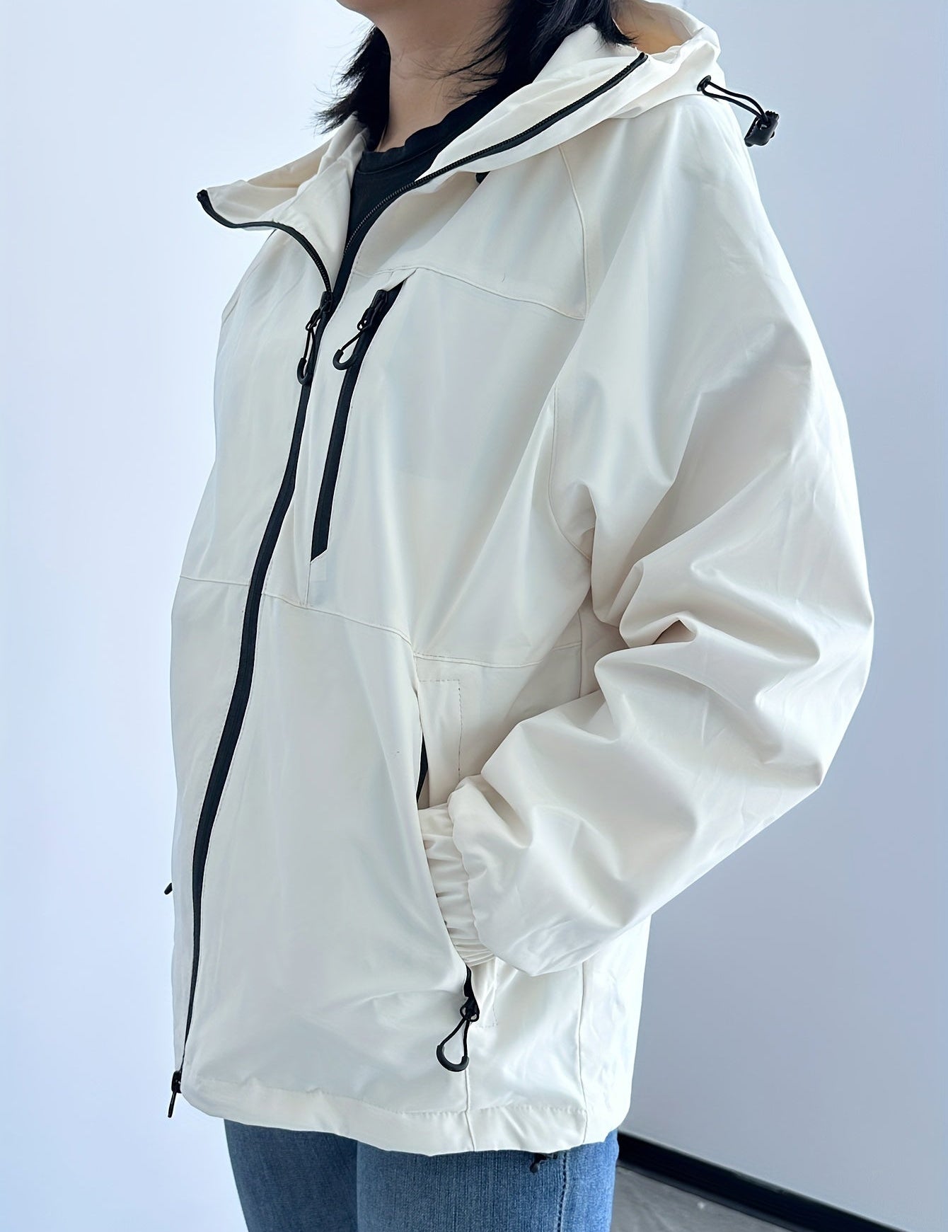 Giacca a vento bianca da donna con cappuccio, zip frontale e tasche laterali, ideale per escursioni e attività outdoor. Stile casual e funzionale.