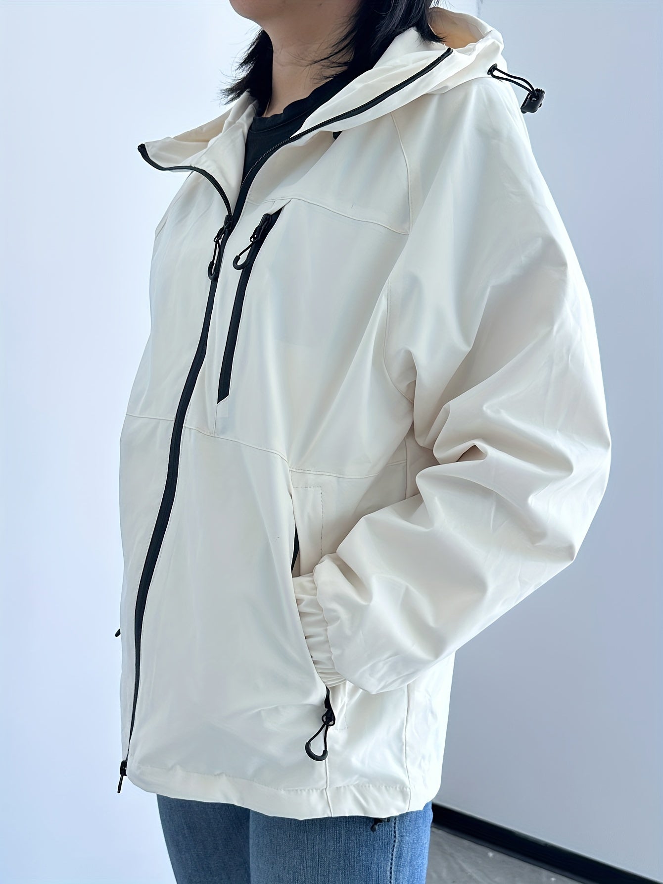 Giacca a vento bianca da donna con cappuccio, zip frontale e tasche laterali, ideale per escursioni e attività outdoor. Stile casual e funzionale.