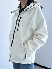 Giacca a vento bianca da donna con cappuccio, zip frontale e tasche laterali, ideale per escursioni e attività outdoor. Stile casual e funzionale.