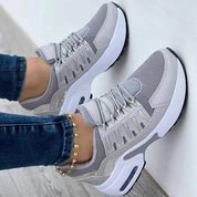 Scarpe da ginnastica grigie e bianche da donna, design moderno, suola ammortizzata, indossate con jeans. Sneakers casual comode e alla moda.