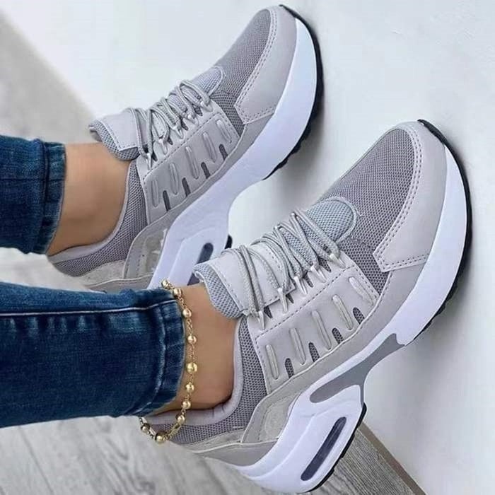 Scarpe da ginnastica grigie da donna, design moderno, suola bianca ammortizzata, indossate con jeans. Sneakers casual eleganti e comode.