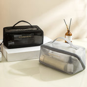 Due beauty case trasparenti su un tavolo, uno nero e uno grigio, contenenti prodotti per la cura personale. Design elegante e pratico per viaggi.